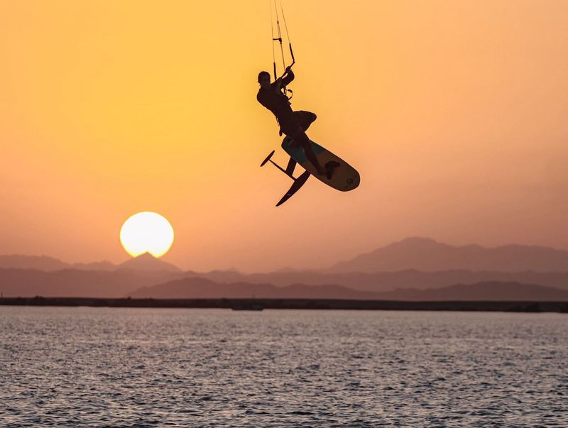Kite foil jump silhouetted against an orange sky
