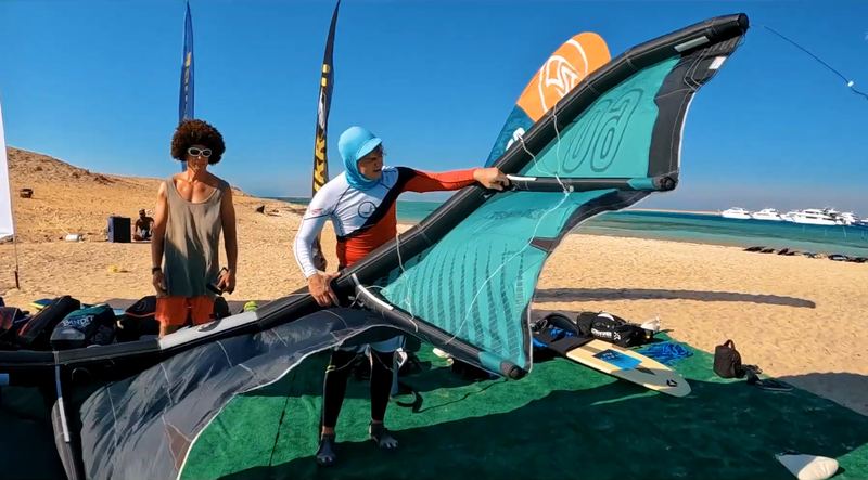 The crew setting up a kite on the beach, yachts on the sea behind