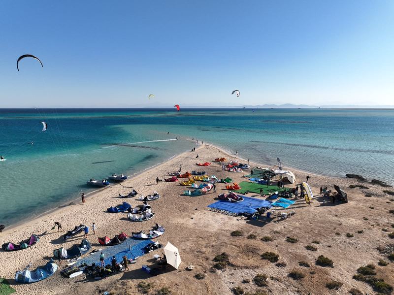 Aerial view of a sandy island spit with kites rigged on the beach and turquoise shallow water