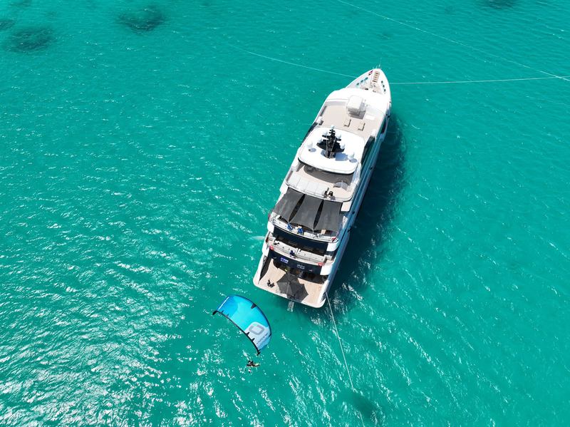 Safari yacht anchored in turquoise water seen from above, a kite in the air next to it